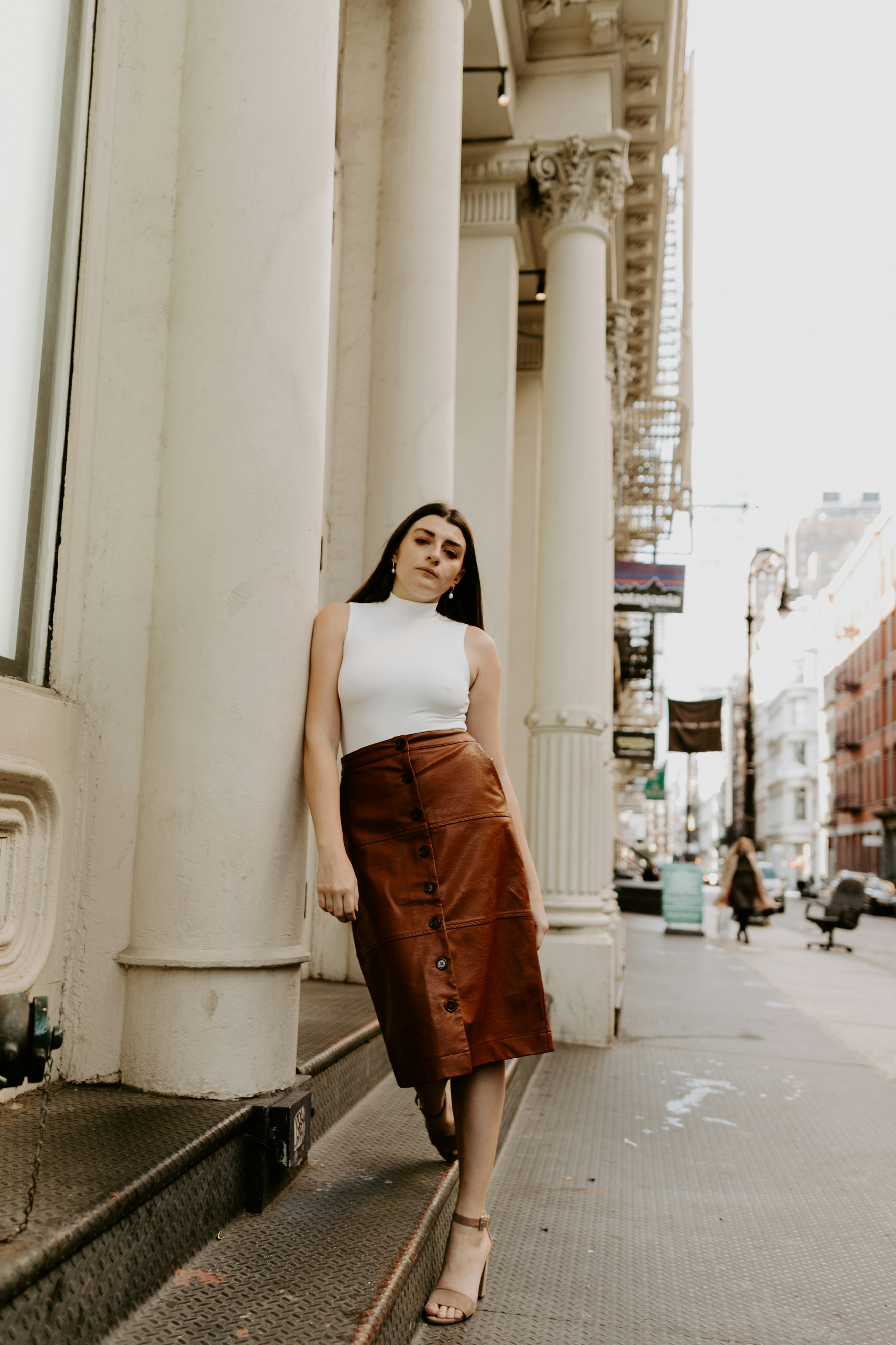 woman in white tank top and brown skirt standing on sidewalk during daytime